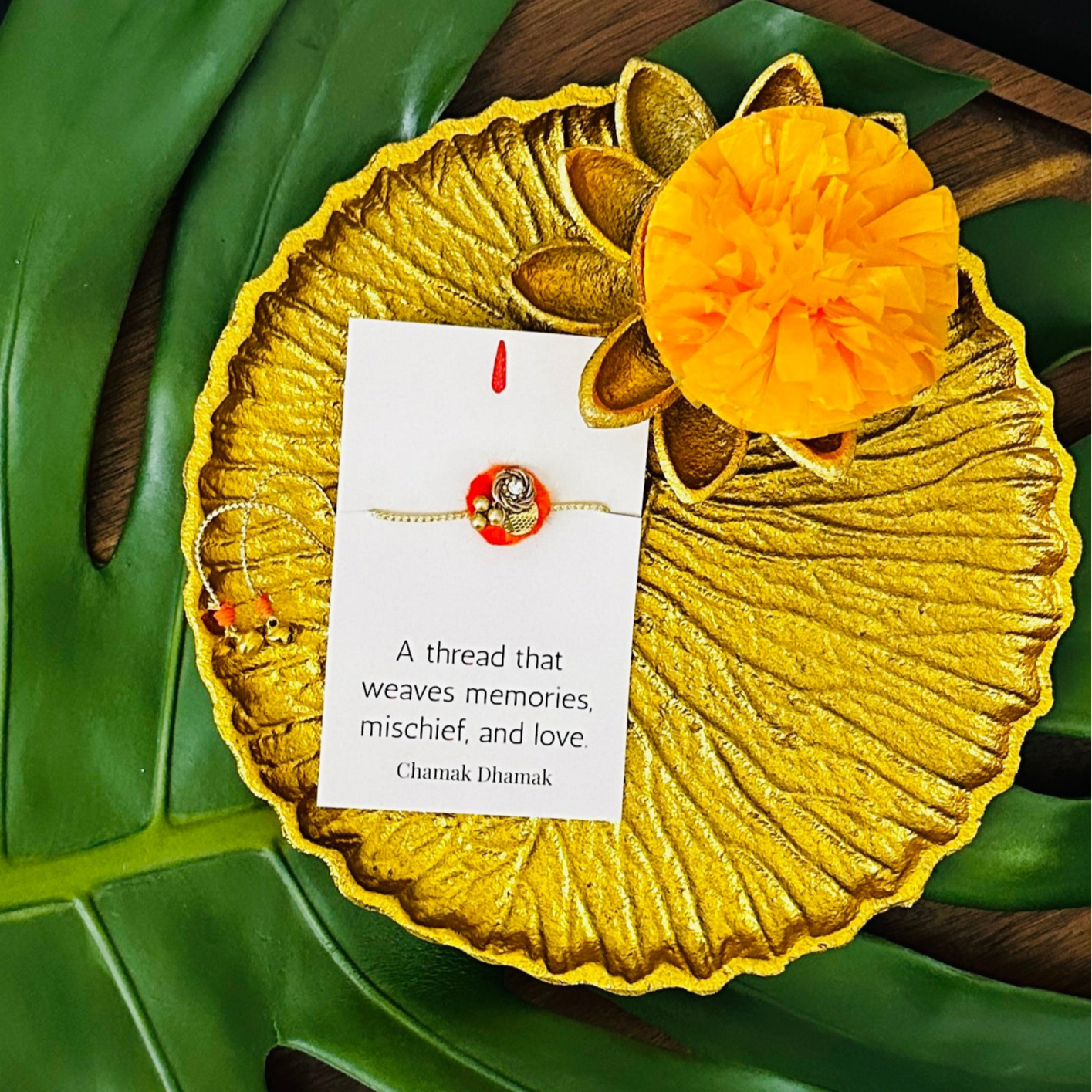 Gold thali with rakhi and marigold flower on a green leaf background
