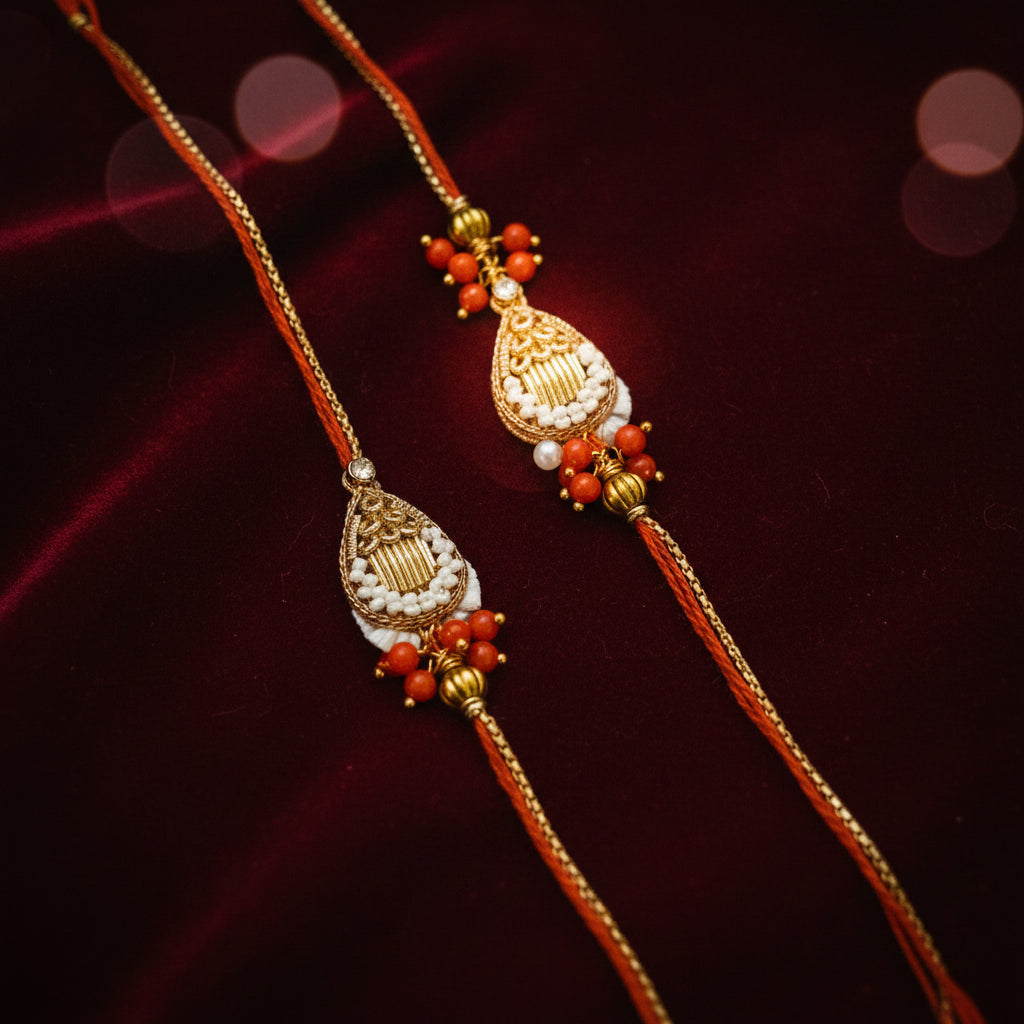 A pair of traditional Indian Rakhi bracelets displayed on a textured white flower-shaped surface. The bracelets feature gold-plated filigree pendants adorned with white beads, small gold beads, and red coral-like beads, connected by red cords.